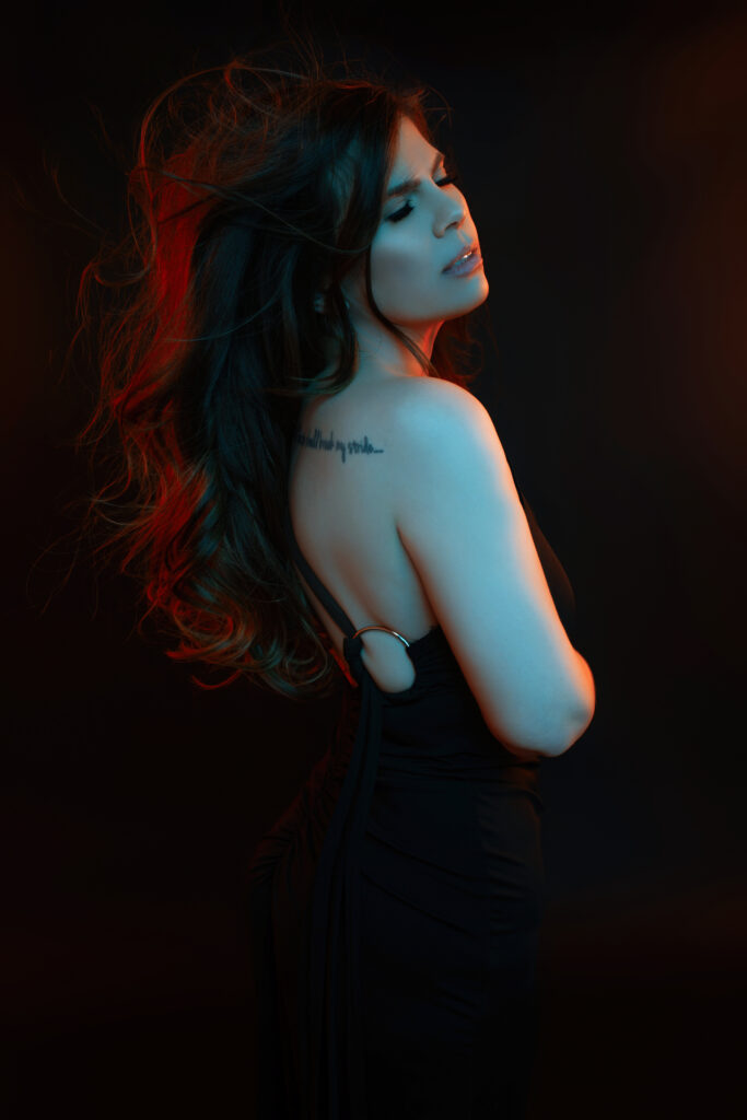 Dark editorial portrait of a woman lit with colored gel lights during an intimate studio session in Oklahoma City.