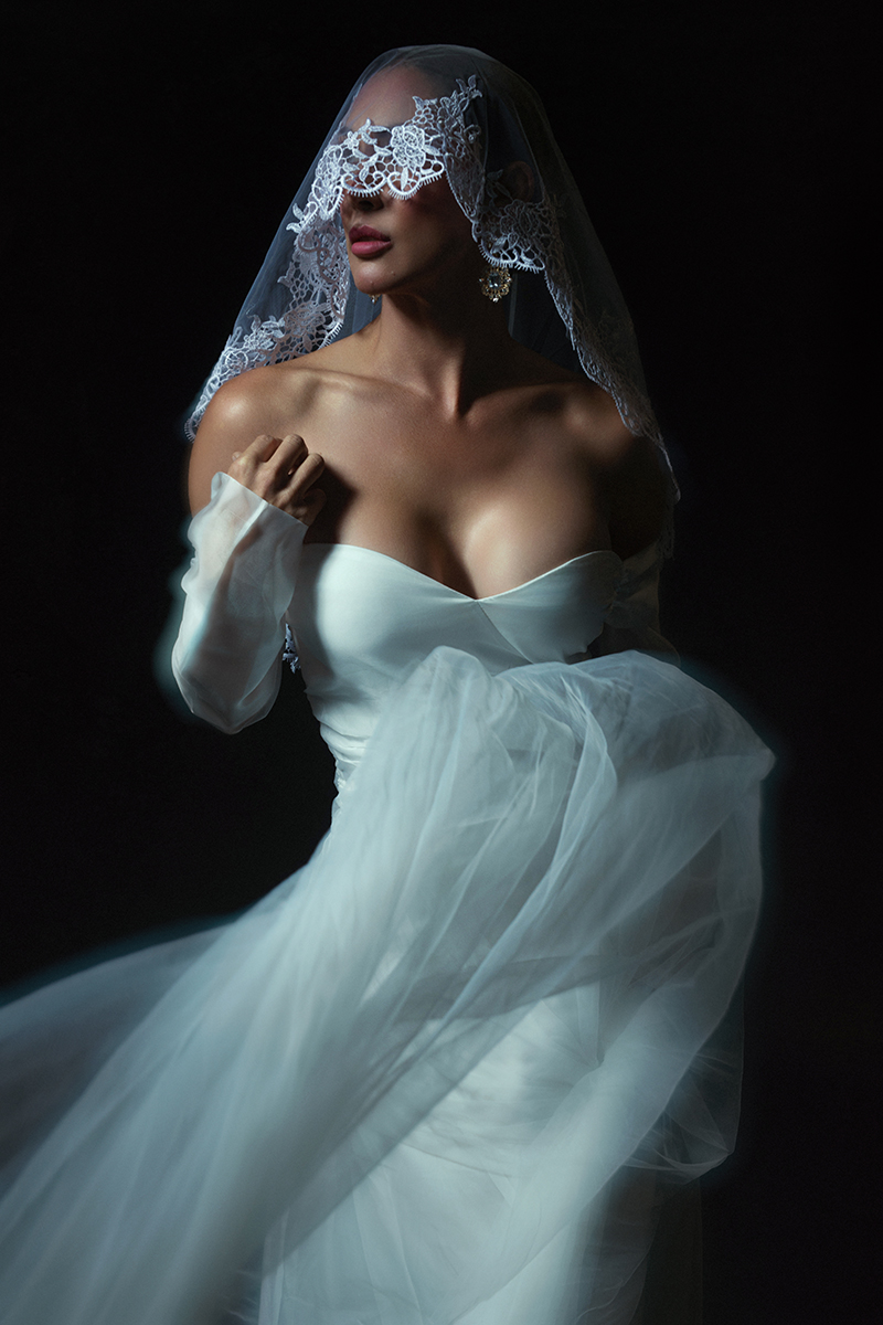 Editorial bridal portrait of a woman in a white gown and lace veil photographed against a dark backdrop in Oklahoma City.
